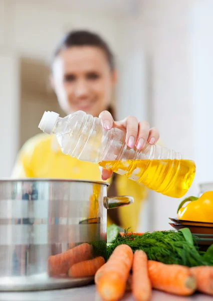 Woman pouring oil from bottle into the saucepan — Stock Photo, Image