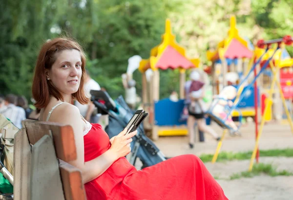 Woman reads e-book against playground area — Stock Photo, Image
