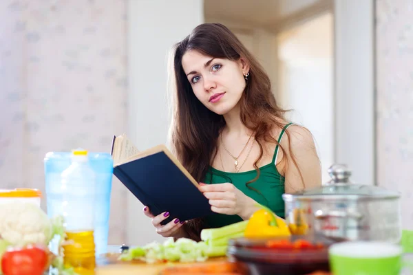 Beautiful woman reads cookbook for recipe — Stock Photo, Image