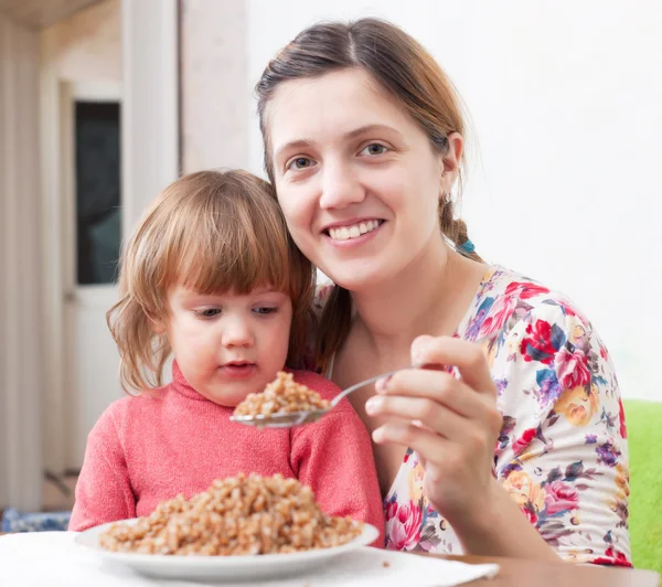 Happy woman with child eats buckwheat — Stock Photo, Image