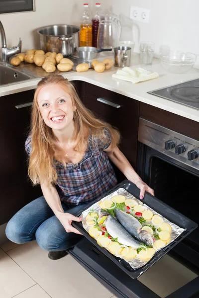 Happy woman cooking raw fish in oven — Stock Photo, Image