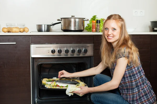 烹饪海鱼在厨房的烤箱里的女人 — 图库照片