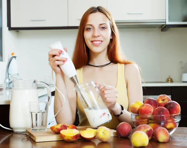 Pitkäkarvainen nainen, joka valmistaa maitojuomia persikoiden kanssa — kuvapankkivalokuva