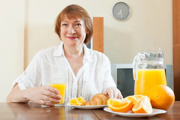 Positive mature woman having breakfast with croissants — Stock Photo, Image