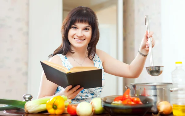 Positieve huisvrouw koken met boek — Stockfoto