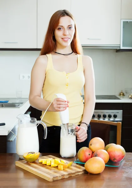 Jonge vrouw bereiding van dranken met blender van mango — Stockfoto