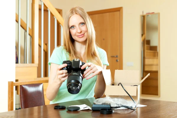 Lachende jonge blond houdt nieuwe digitale camera in huis interieur — Stockfoto