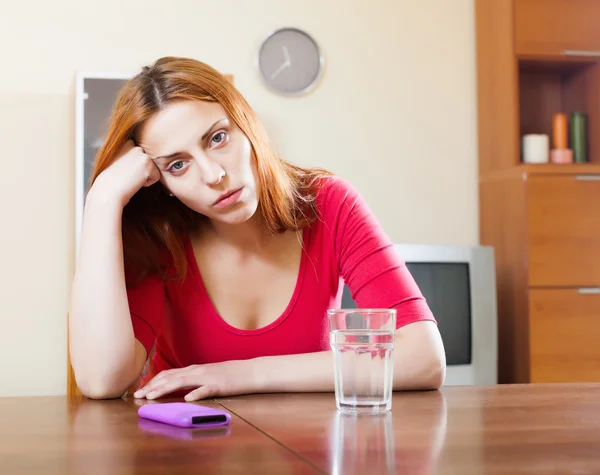 Плачущая женщина с мобильным телефоном за столом — стоковое фото