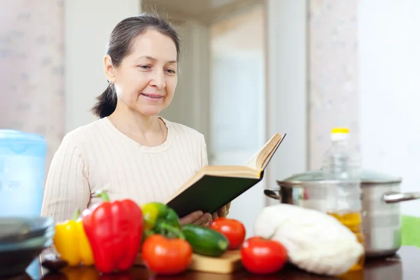 Starší žena v domácnosti cook s knihou — Stock fotografie