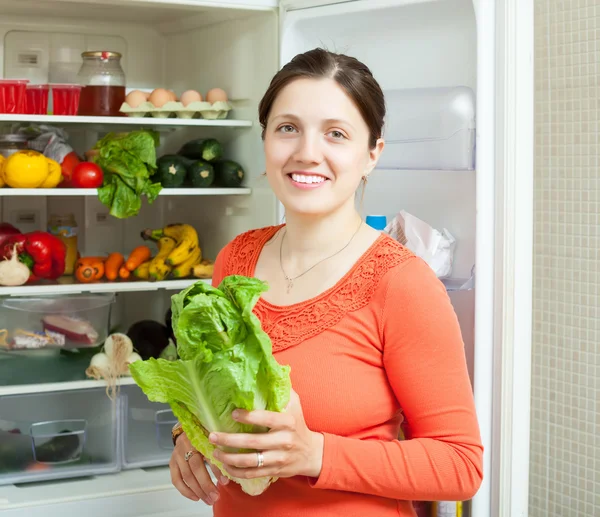 Happy woman putting vegetables into refrigerator — Stock Photo, Image