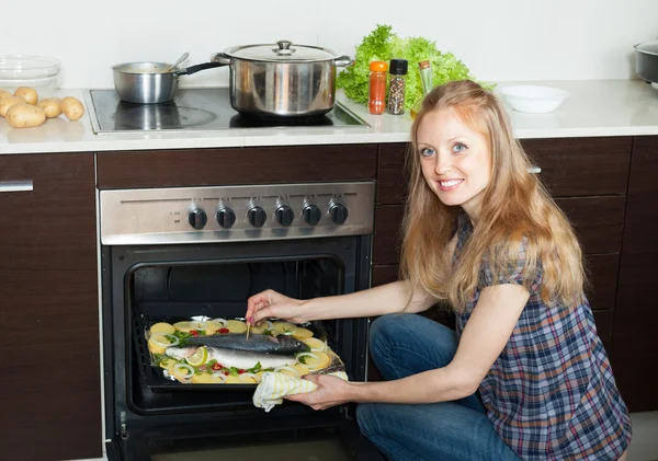 Улыбающаяся домохозяйка готовит морскую рыбу и картошку на листе p — стоковое фото