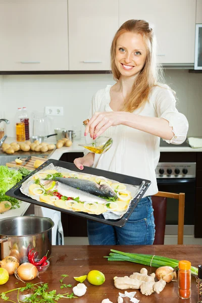 Mujer feliz vertiendo aceite en el pescado — Foto de Stock