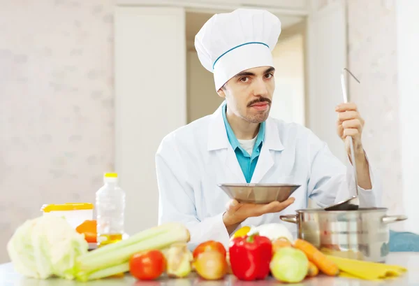 Chef pours vegetables soup from pan to plate — Stock Photo, Image