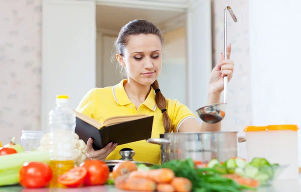 Mujer cocina comida con libro — Foto de Stock