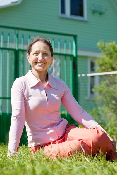 Happy woman sitting against home — Stock Photo, Image