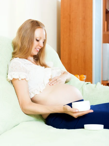 怀孕美丽的女人，施加在家里的床上腹部的奶油 — 图库照片