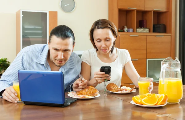 Casal feliz usando dispositivos eletrônicos durante o café da manhã — Fotografia de Stock