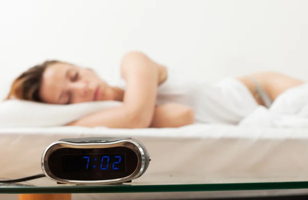 Alarm clock by the bad of sleeping woman — Stock Photo, Image