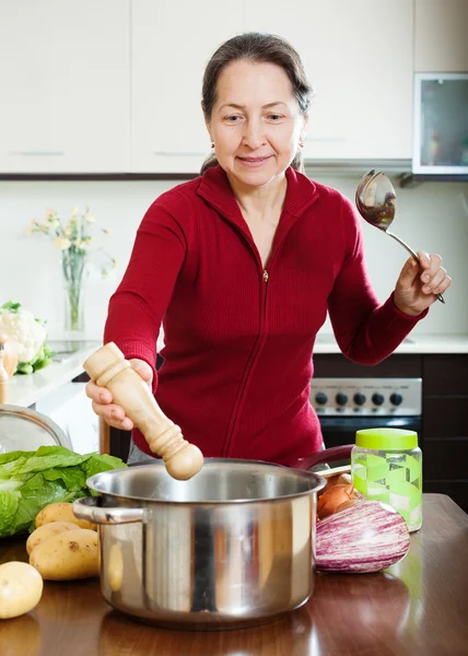 Mature woman adding seasoning into pan — Stock Photo, Image