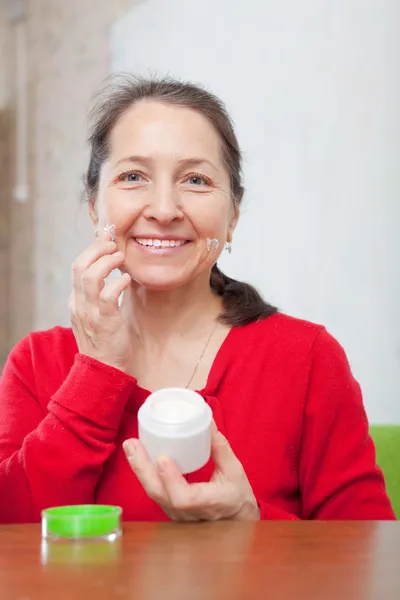 Mulher madura coloca creme no rosto — Fotografia de Stock