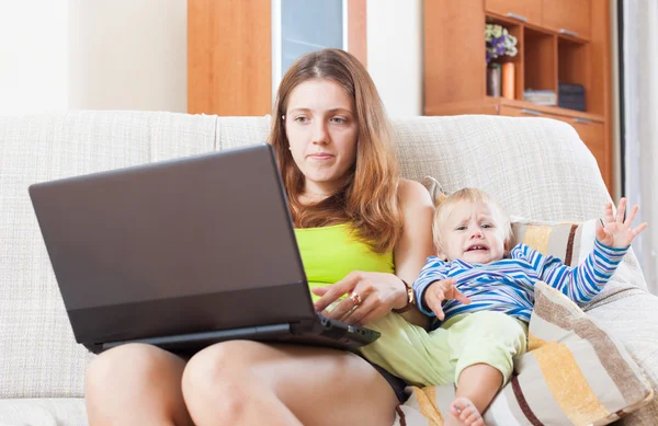 Sorehead mãe com choro criança trabalhando online — Fotografia de Stock