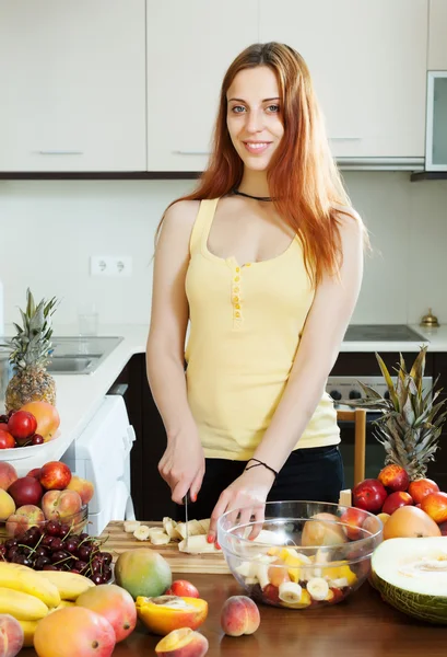 Feliz joven mujer cortando frutas para ensalada — Foto de Stock