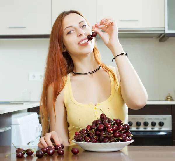 Menina comendo cerejas na cozinha — Fotografia de Stock