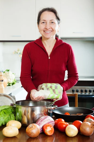 Smiling mature woman cooking soup with rice — Stock Photo, Image