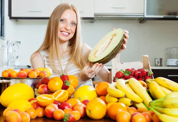 Gelukkig blonde vrouw in de buurt van heap van vruchten op huis keuken — Stockfoto