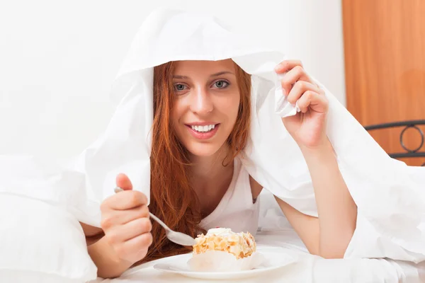 Glückliche Frau isst süßen Kuchen unter Laken — Stockfoto