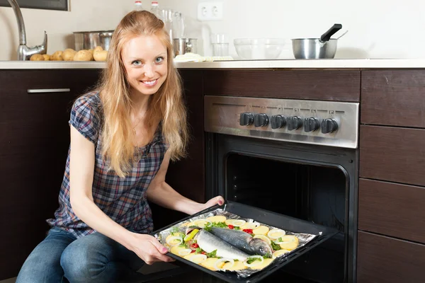 Smiling girl cooking raw fish in oven — Stock Photo, Image