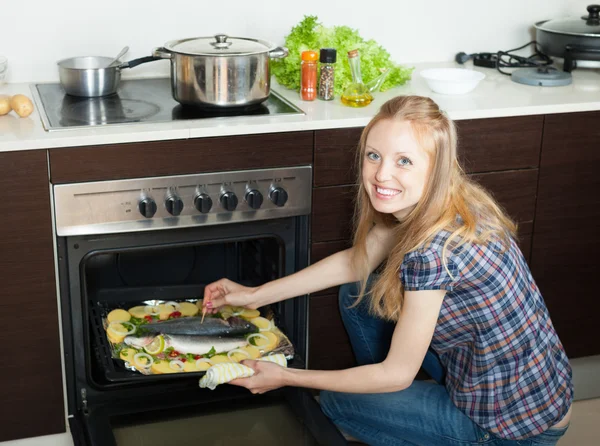 Positive woman cooking fish in oven at kitchen — Stock Photo, Image