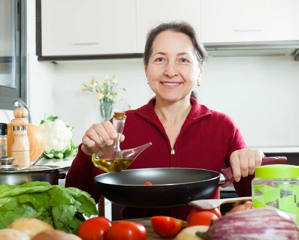 Gelukkig volwassen vrouw olie gieten in koekepan — Stockfoto