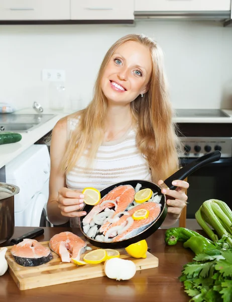 Smiling woman putting pieces lemon in fish — Stock Photo, Image