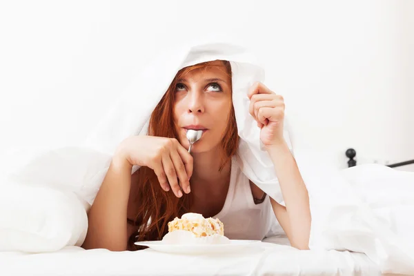 Menina ruiva comendo biscoito na cama — Fotografia de Stock