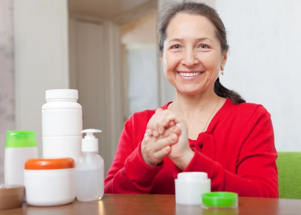 Mujer madura en rojo aplicando crema en las manos — Foto de Stock