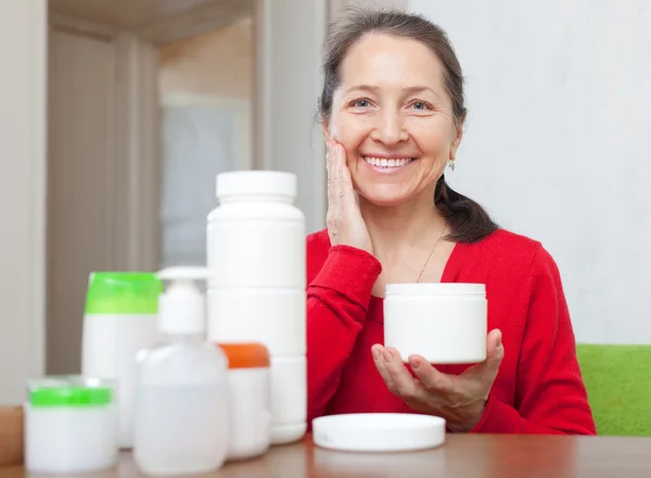 Happy mature woman puts cream on face — Stock Photo, Image