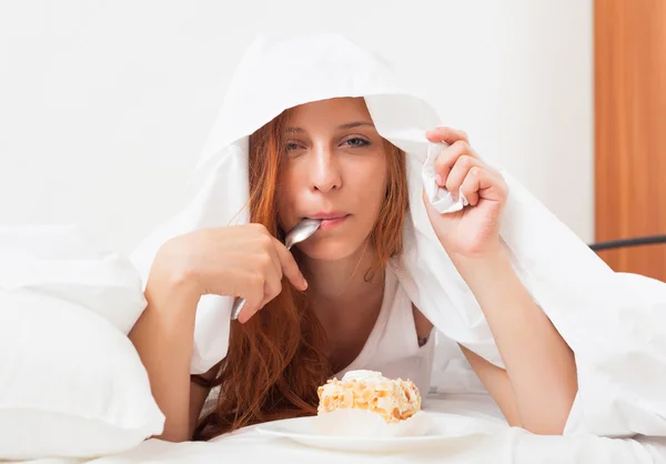 Mujer comiendo pastel dulce bajo sábana — Foto de Stock