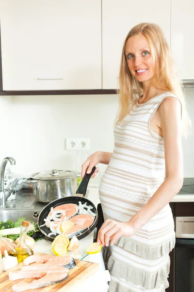 Sorridente donna incinta cucina salmone — Foto Stock