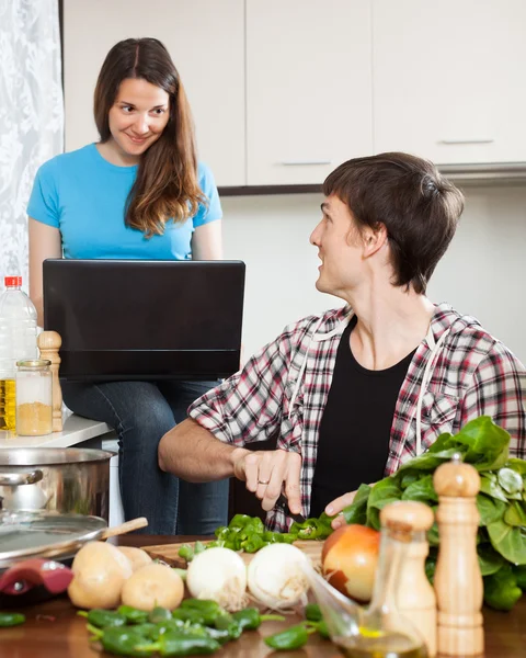 Mens koken voedsel terwijl vriendin kijken naar laptop — Stockfoto