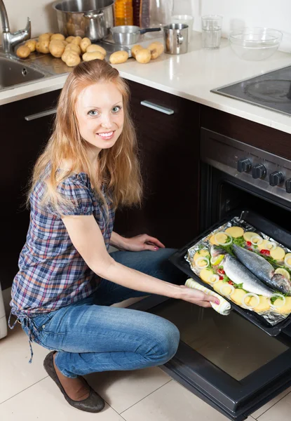 Улыбающаяся женщина готовит сырую рыбу в духовке — стоковое фото
