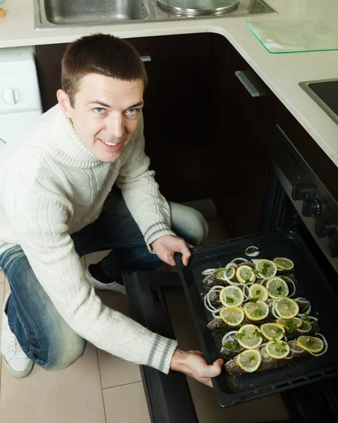 Man putting  fish on roasting pan into oven — Stock Photo, Image