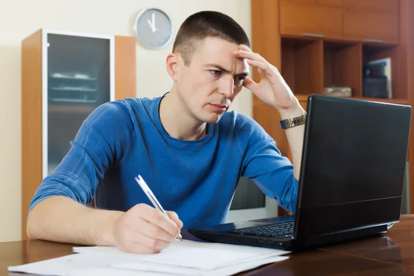 Mann starrt Finanzunterlagen in Laptop — Stockfoto