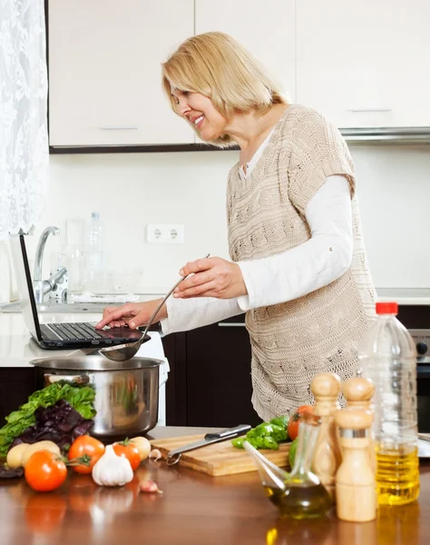 Vrouw met laptop tijdens het koken — Stockfoto