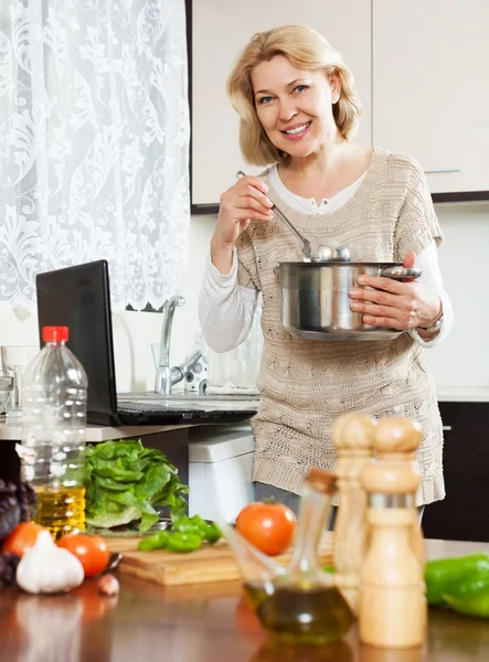 Домохозяйка с помощью ноутбука во время приготовления супа — стоковое фото