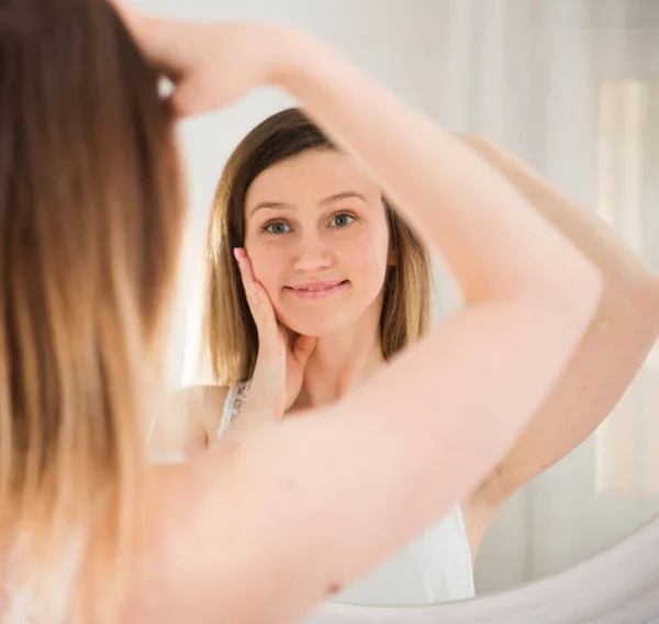 Portret van meisje aanraken gezicht en kijken naar spiegel in de slaapkamer — Stockfoto