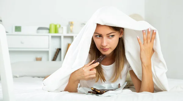 Frau isst Schokolade im Bett — Stockfoto