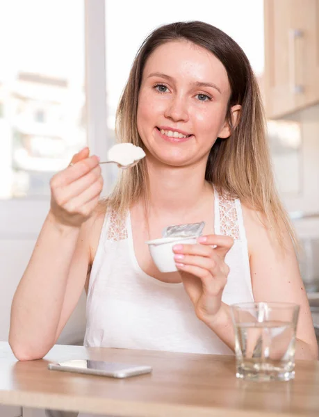Portret wesołej kobiety, która zabawnie pozuje z jogurtem przy stole — Zdjęcie stockowe