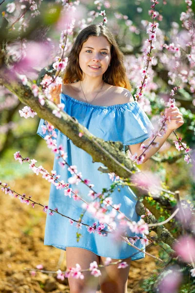 Dívka v jarní zahradě broskev v modrých šatech — Stock fotografie