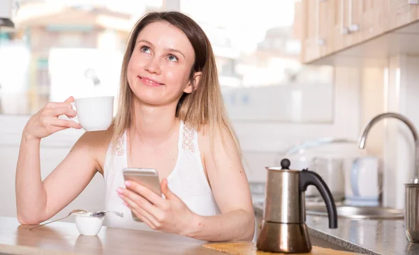 Meisje is chatten op de telefoon en het drinken van thee aan tafel en geluk alleen — Stockfoto